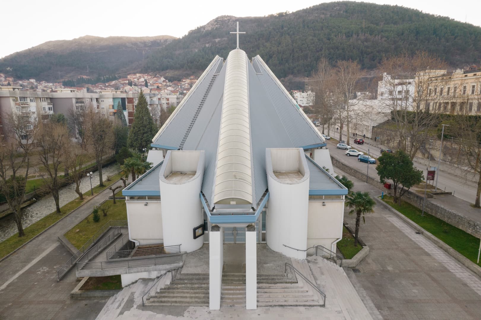Mostarska katedrala snimljena iz zraka: središnji stup s križem i krovne plohe, iza grad i brdo